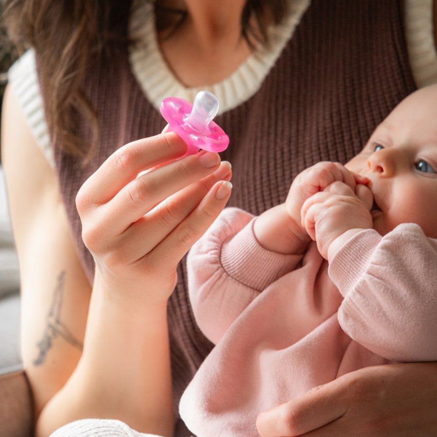 A parent offering a pink Minbie pacifier