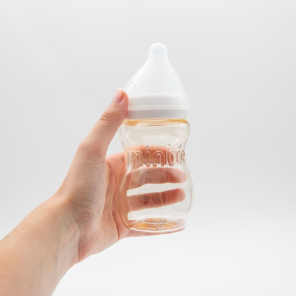 A hand holding a clear Minbie PPSU bottle