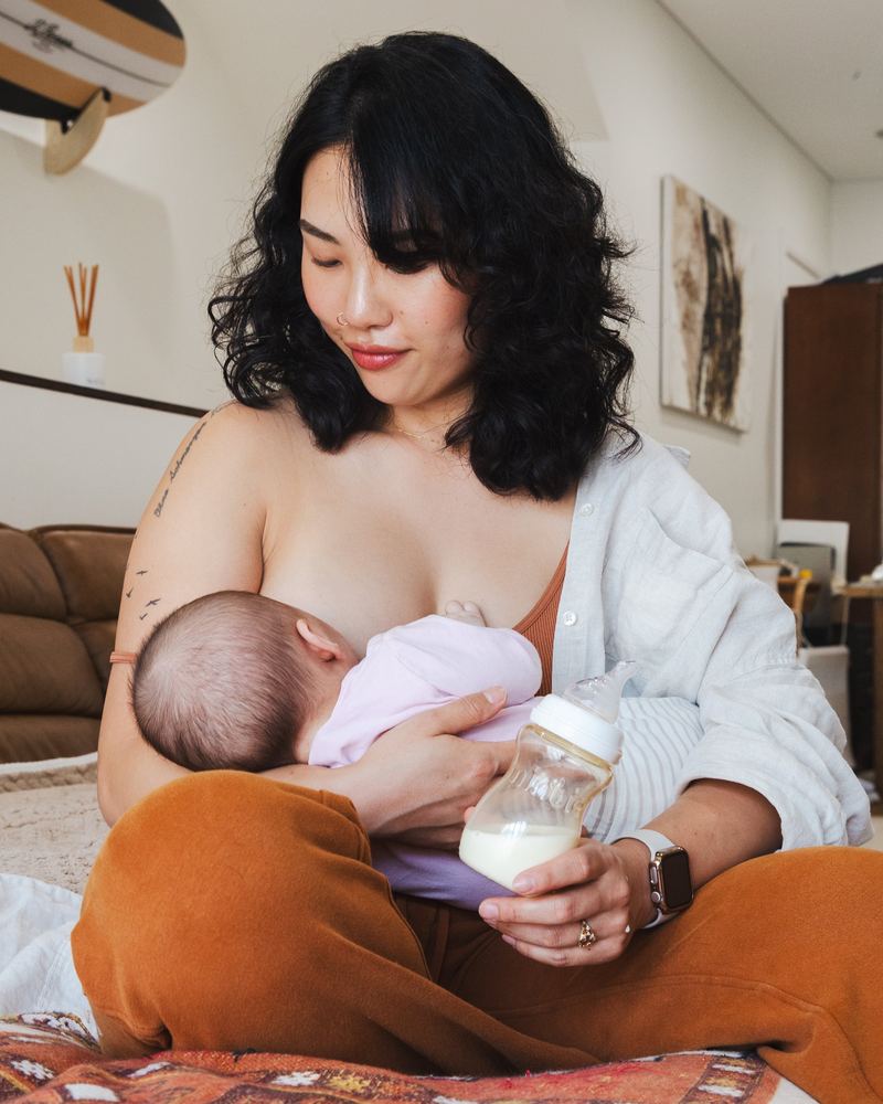 A mom breastfeeding while holding a Minbie bottle