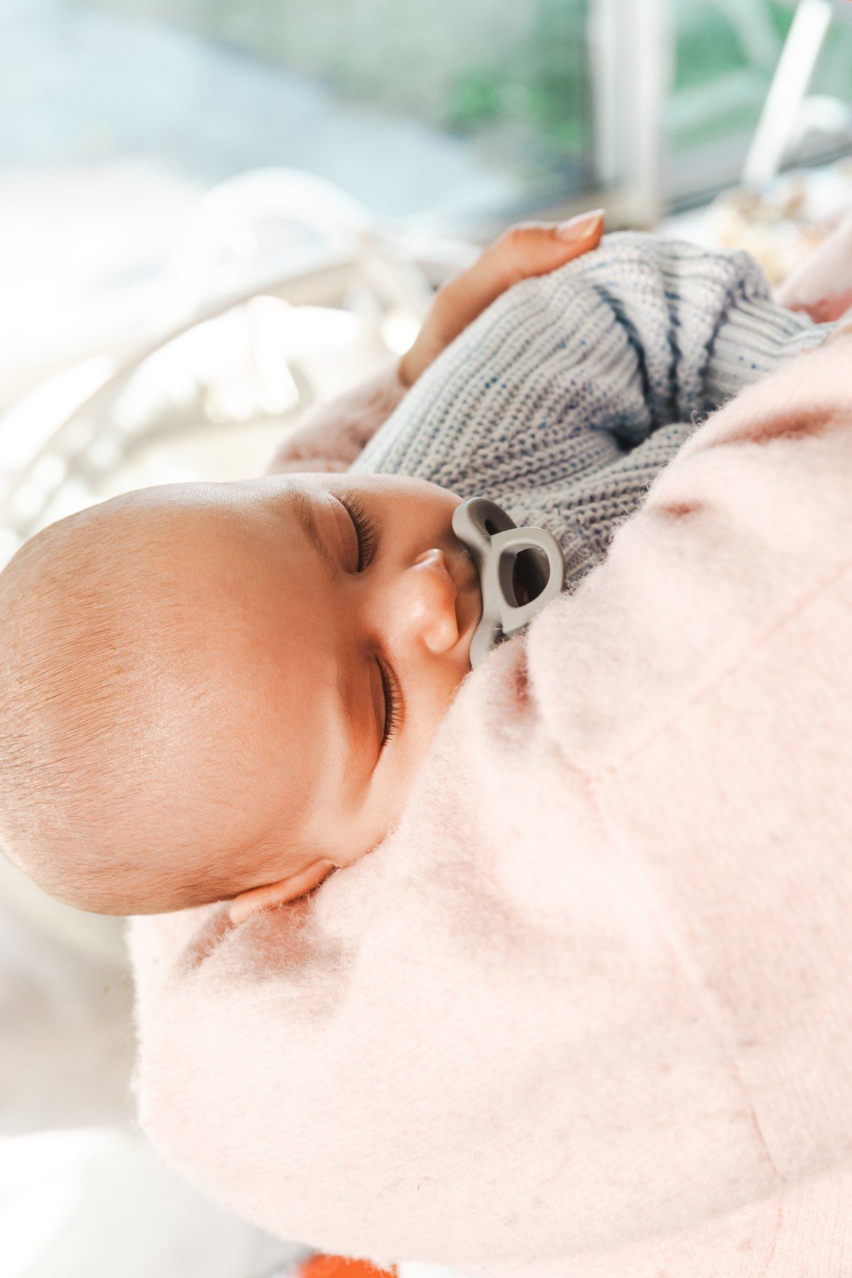 A baby resting on a parent’s chest with a gray Minbie pacifier