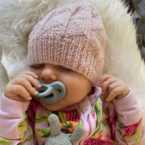 A baby in a knitted hat with a Minbie pacifier
