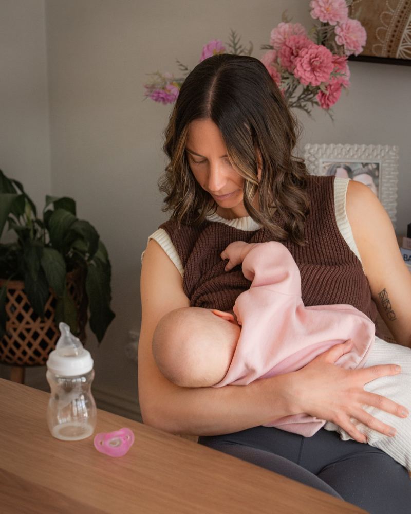 A mom breastfeeding with a Minbie bottle and pink pacifier on the table